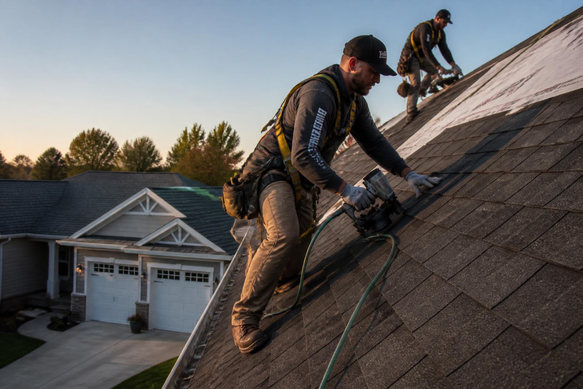 Roofing crew installing architectural shingles at sunset